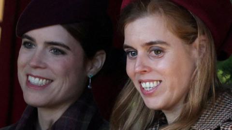 Princesses Eugenie and Beatrice, seen in close-up, smiling and looking off camera - they are both wearing coats and hats 