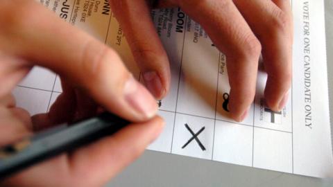 Hand holding a pen over a ballot paper with a cross marked on it