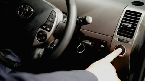A person sat in the driver's seat of a car pressing a button to start the engine