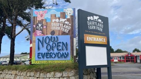 The entrance to Dairyland. A stone wall can be seen with two signs, one saying "Entrance" and the other saying "Now open every day"