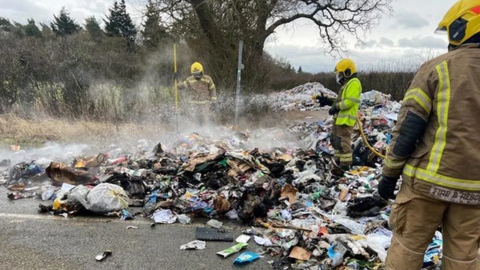 Three firefighters look at a smouldering pile of rubbish which was dumped on a Lincolnshire road when a bin lorry set alight.