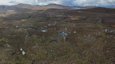 An aerial photograph showing a wide open expanse of peat bog. There are dozens of small pools and very few trees.