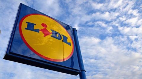 A shiny blue, yellow and red Lidl supermarket sign with a blue sky with some white clouds in the background