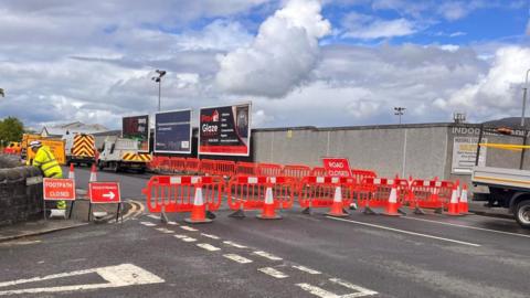 A section of road outside a football stadium. The road is closed with signs indicating this and red barriers placed across the road