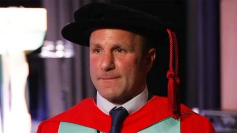Willie Peters wearing his red and green ceremonial robe and a black cap with a red tassle