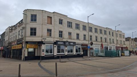 A site of a former hotel with empty floors over a bar and some shops.