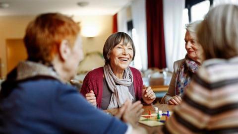 A group of older women playing a board game and sitting round a table together