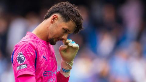 Manchester City goalkeeper James Trafford touches his face with his left glove
