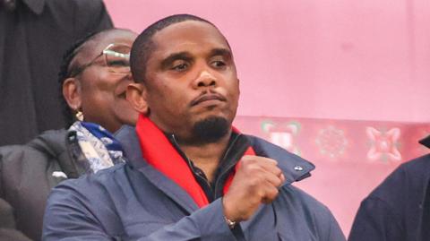 Samuel Eto'o raises his right fist while seen in the stands at a football match