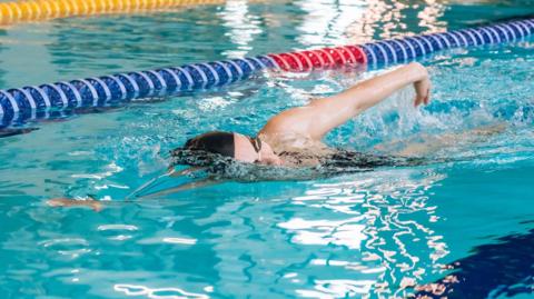 A woman in a black swimming cap and goggles swims freestyle along a lane marked by a red and blue line
