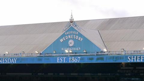 A view of the top of the stand at Hillsborough with Sheffield Wednesday written in curvature across it, just above a clock and with the words 'Est. 1867' below that 