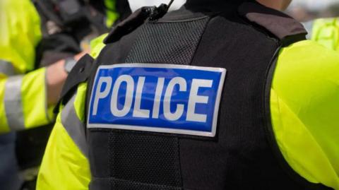 The back of a person wearing a black police vest with the word POLICE written in white on a blue background