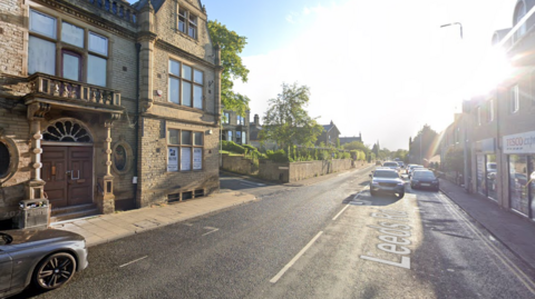 A single carriageway high street with a decorative building on the left and a Tesco Express on the right.