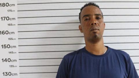 Mohammed Tahir aka "Wordi" in a navy T-shirt stands against a measuring chart in a police photo - putting his height at around 178cm.