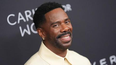 Colman Domingo at Kering Foundation Fourth Annual 'Caring for Women' Dinner in New York at The Pool on September 11, 2025 in New York, New York. He appears smiling at the camera, wearing a cream-coloured collared shirt and a gold earring.
