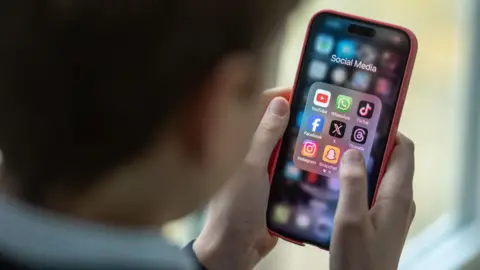 Bachgen ifanc yn gafael Iphone, yn dangos apps cyfryngau cymdeithasol