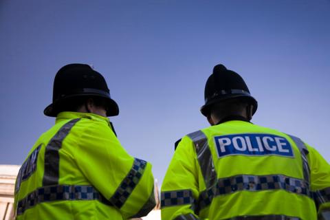 British Police officers wearing yellow high vis jackets. Shot of the back of a couple of British Police officer's reflective jackets with the word POLICE written across the back. 