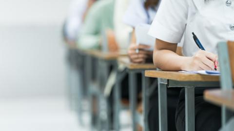 Students Taking Exam in Classroom Setting. Students in uniforms are seated in a classroom, writing answers during an exam, highlighting focus and academic testing. - stock photo