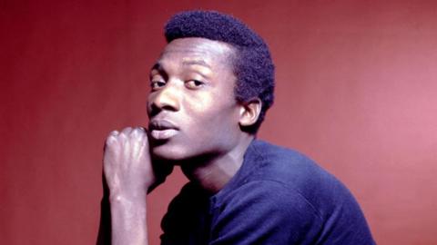 Jimmy Cliff staring sideways at the camera, wearing a navy blue sweater.