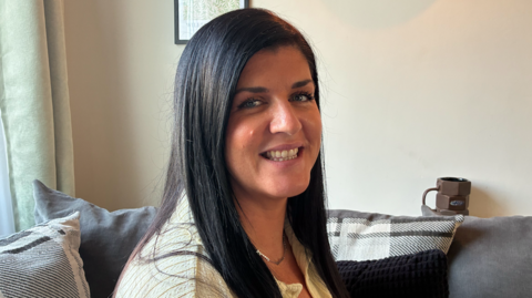 A woman with long brown hair sat on a sofa.