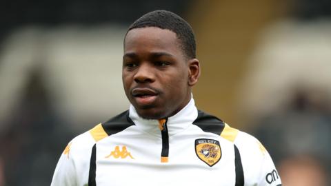 A close-up of Eliot Matazo in a white, black and orange Hull City warm up top