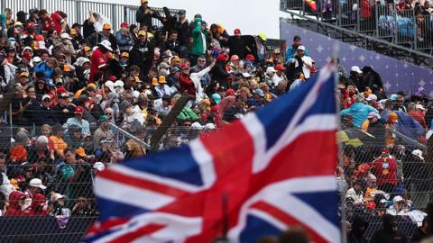 Fans watch on the from the grandstand at Silverstone with a Union Jack flag in the foreground 
