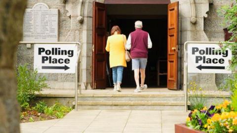 A man and a woman walking into a polling station in a church.