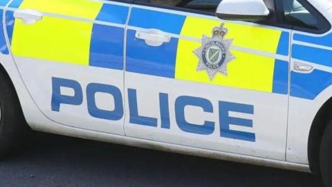 Side view of a marked Lincolnshire Police car. It is white with yellow and blue blocks and the force's badge on the door.
