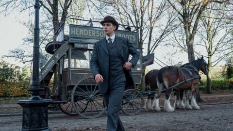 A man in a suit in front of horses and a cart