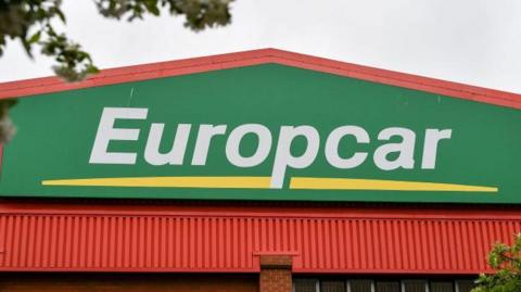White lettering which says Europcar on a green background and over a yellow line, on a building.
