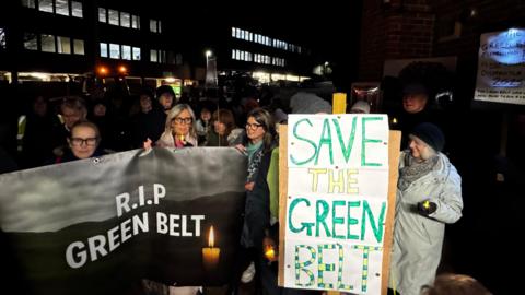 Protestors hold signs outside a council meeting, reading ' R.I.P GREEN BELT' and 'SAVE THE GREEN BELT'