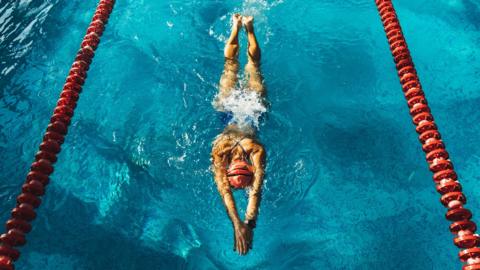 An overhead shot of a woman swimming in a lane of a swimming pool while wearing a swimsuit and cap