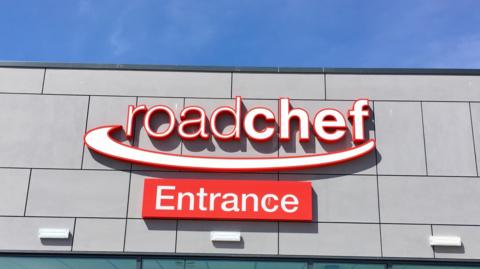 Front view of a red and white Roadchef sign. An additional sign that reads "Entrance" is mounted below.