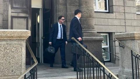 A man wearing a suit and sunglasses exiting the Royal Court.