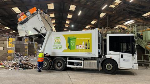 A bin truck unloads glass at a recycling plant.