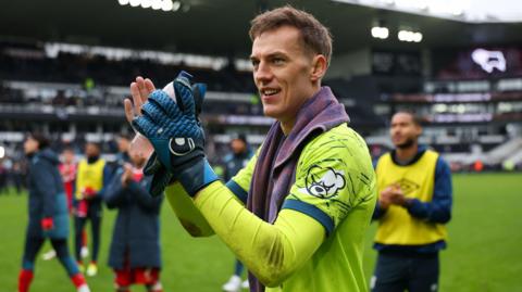 Ipswich goalkeeper Christian Walton applauds fans with one glove on and carrying other at end of a victory