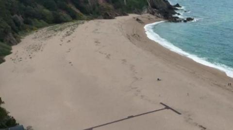 An aerial view of a white sandy beach surrounded by cliffs