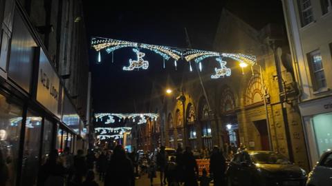 Christmas lights hanging in St Helier Jersey with people walking on the road in the dark.