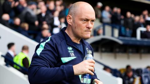 Alex Neil drinks from a bottle of water and looks focused on the Millwall touchline