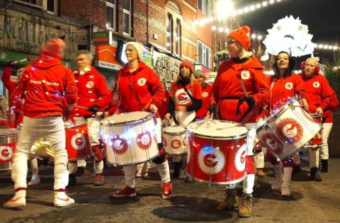 Members of a Bristol samba band lead the Bedminster Winter Lantern Parade, all of them wearing red hoodies and white trousers. Some are carrying large drums