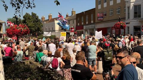 A crowd of people in a high street, with several banners and union flags flying
