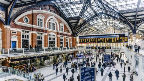 The inside of Liverpool Street station. It has a glass ceiling and a notice board showing the train times. 