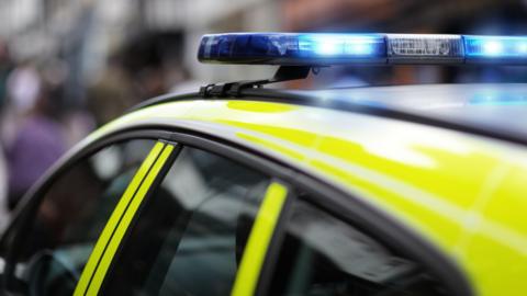 A stock image of a police siren flashing blue lights at an accident or crime scene. It is on top of a bright yellow police vehicle. 