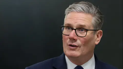 Starmer gestures with right hand while speaking in front of two microphones
