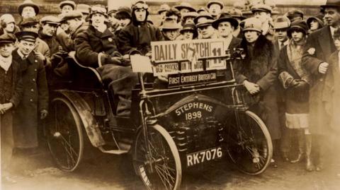 A crowd of people gathered around a Stephens car