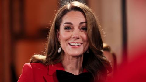 The Princess of Wales smiles at the camera, wearing a red coat and black bow