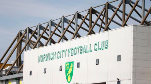The exterior of a football stadium is shown, with the club's name and crest in large letters on white panels.
