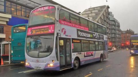 A number 34 bus bound for Leeds Bus Station drives down a wet city centre street.