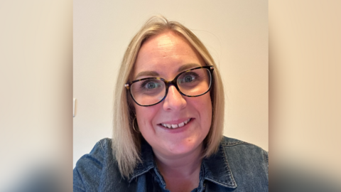 A blonde women with glasses smiling at the camera in selfie mode.