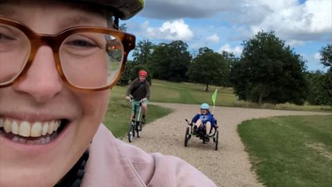 Lady takes a selfie with a girl in an adapted bike behind her
